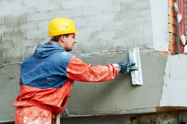 Stucco repair worker applying plaster to an exterior wall, illustrating professional stucco repair before exterior painting in Polk County, FL.